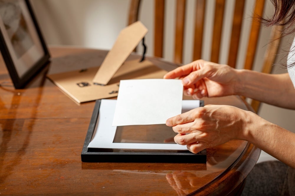 person placing photo in small frame with matting