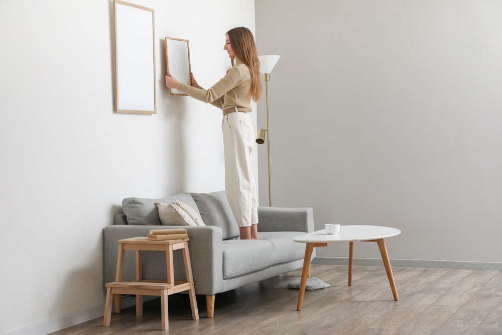 woman standing on couch hanging frame on wall