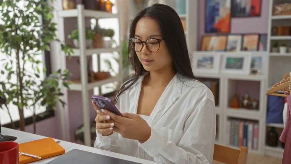 Young chinese woman using phone in a brightly decorated home decor shop with various home decor items on shelves in the background.